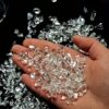 A hand holding a handful of sparkling, clear quartz demagnetizing stone chips against a black background to show their quality.