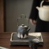A close-up detail shot of the ornate, silver-accented lid of a handmade ceramic teapot, showing its fine craftsmanship.