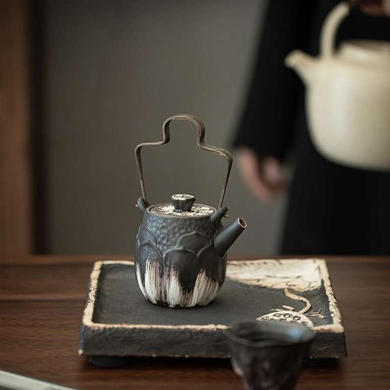 A close-up detail shot of the ornate, silver-accented lid of a handmade ceramic teapot, showing its fine craftsmanship.