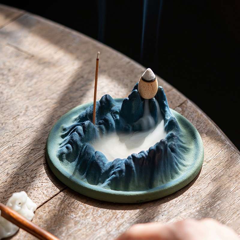 The mesmerizing smoke waterfall effect of the backflow incense burner, with thick, milky smoke pooling in the valleys of the mountain design.