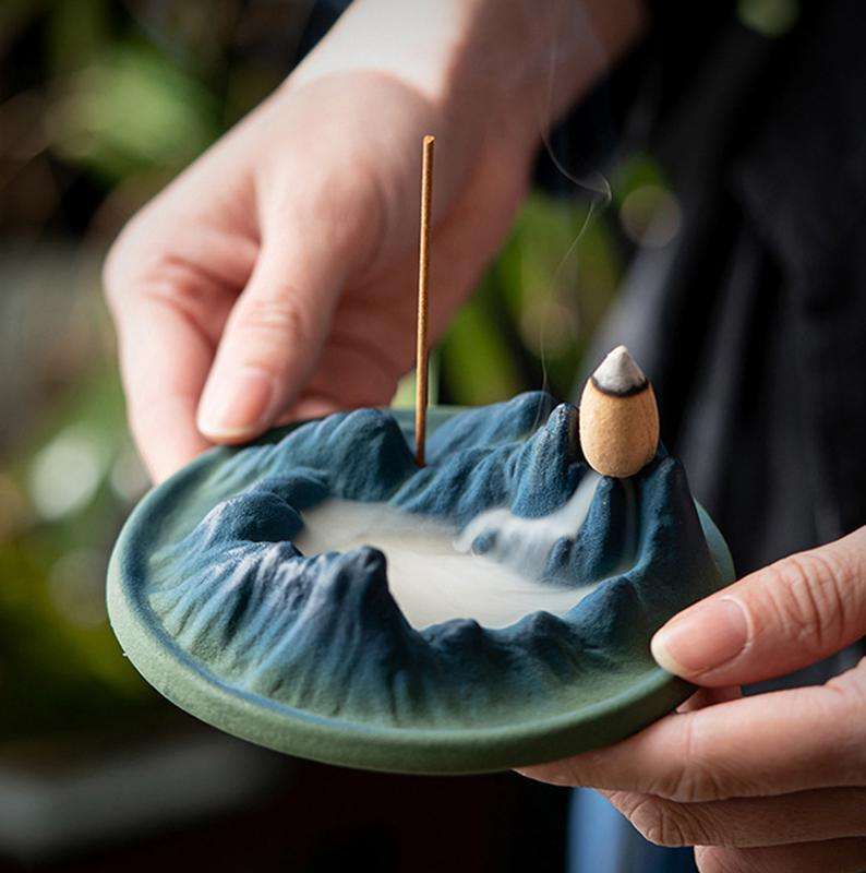 A close-up of a backflow incense cone placed on the peak of the mountain style burner, just as the smoke begins to cascade downwards.