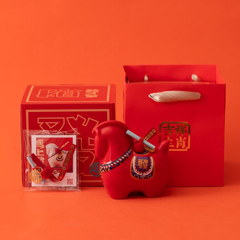 Close up of a red year of the horse ceramic ornament showing the golden coin detail, greeting scroll, and glossy porcelain finish for Lunar New Year decoration.