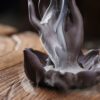 Zen style Buddha hand backflow incense burner placed on a wooden tea table with stick incense burning, creating a meditative atmosphere.